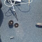 Przyrządy pomiarowe na szarej powierzchni dachowej obok dwóch okrągłych próbek materiału