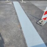 Świeżo namalowana jasnoniebieska linia na jezdni obok ciężarówki i tymczasowych znaków drogowych