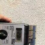 Cyfrowy wilgotnościomierz do betonu przyłożony do jasnej ściany pokazuje wynik 2,8% H2O