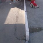 Pracownik drogowy w pomarańczowym stroju klęczy i uszczelnia szczelinę w betonowej nawierzchni