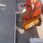 Pracownik budowlany w kasku i kamizelce odblaskowej klęczy przy szczelinie w betonowej posadzce