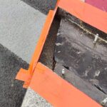 Prace drogowe przy przejściu dla pieszych: otwarty właz zabezpieczony pomarańczową taśmą, obok wiertarka i świeży asfalt