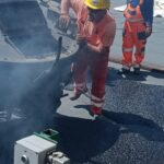 Robotnicy w odzieży odblaskowej układają gorący asfalt z dymiącej maszyny drogowej