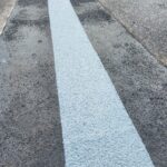 Jasnoniebieski, chropowaty pas na ciemnym asfalcie przy ogrodzonym placu budowy