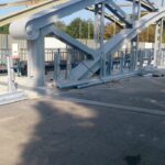 Stalowa konstrukcja mostu w trakcie montażu, z barierkami i żółtym vanem po prawej stronie