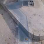 Betonowy cokół z zaokrąglonym narożnikiem i metalowymi śrubami u góry, sfotografowany z bliska na zewnątrz