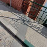 Kamienne schody przy czerwonym ceglanym murze i łuku, z zieloną poręczą nad wodą