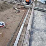 Pracownik w kamizelce odblaskowej montuje zbrojenie przy betonowym nabrzeżu na placu budowy