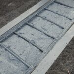 Wąski świeżo wylany betonowy pas ze zbrojeniem w szalunku, otoczony ciemnym żwirem