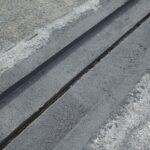 Zbliżenie na ciemne pasy uszczelnienia lub asfaltu na szarej betonowej nawierzchni