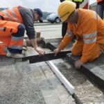 Dwóch robotników drogowych w odblaskowych ubraniach mierzy szczelinę w jezdni podczas naprawy drogi