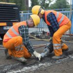 Dwóch robotników drogowych w kaskach i kamizelkach odblaskowych pracuje przy rozkuwaniu nawierzchni jezdni