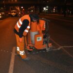 Pracownik drogowy w odblaskowej kamizelce obsługuje maszynę do naprawy nawierzchni na nocnej ulicy