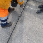 Pracownik drogowy w pomarańczowym stroju uszczelnia szczelinę w betonowej nawierzchni przy krawężniku