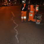Pracownik drogowy nocą uszczelnia pęknięcie nawierzchni jezdni pomarańczową maszyną