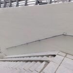 Schody zewnętrzne przy jasnej ścianie z metalową poręczą, prowadzące w dół do przejścia pod wiaduktem