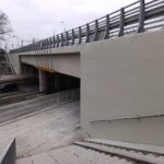 Schody i chodnik prowadzą do przejścia pod wiaduktem nad drogą, obok której jedzie samochód