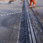Pracownicy drogowi w pomarańczowych strojach naprawiają nawierzchnię przy szynie tramwajowej na jezdni