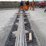 Robotnicy w kaskach naprawiają dylatację na moście, odsłaniając zbrojenie i metalowe prowadnice w jezdni