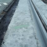 Torowisko tramwajowe w trakcie budowy, obok asfaltowa jezdnia i zielona strzałka namalowana na betonie
