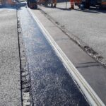 Robotnicy montują dylatację mostową w jezdni, otoczoną świeżym asfaltem i sprzętem drogowym