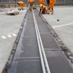Robotnicy w pomarańczowych strojach montują metalową szczelinę dylatacyjną na jezdni mostu
