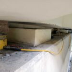 Pracownik na rusztowaniu podnosi ciężki betonowy element siłownikami hydraulicznymi podczas prac konstrukcyjnych