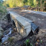 Nowy betonowy mostek na leśnej drodze nad wąskim strumieniem, otoczony ziemią i materiałami budowlanymi