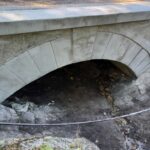 Kamienny łuk małego mostu nad niemal suchym korytem strumienia