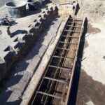 Wykop przy chodniku z szalunkiem i zbrojeniem pod betonowy fundament, obok narzędzia i bloczki
