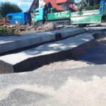 Roboty drogowe przy montażu betonowego kanału odwodnienia, z ciężarówką TARCOPOL i pracownikami w tle