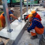 Trzej robotnicy malują i wykańczają betonową podstawę z metalowymi słupami na placu budowy