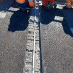 Pracownicy drogowi w pomarańczowych strojach montują dylatację na asfaltowej nawierzchni