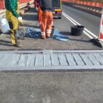Robotnicy naprawiają dylatację na moście, obok narzędzi, wiader i znaku drogowego