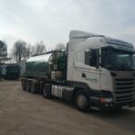 Biała ciężarówka Scania TARCOPOL z cysterną stoi na placu firmy, w tle widać inne ciężarówki