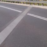 Jezdnia mostu z podwójną linią ciągłą i szerokim ukośnym oznakowaniem na asfalcie